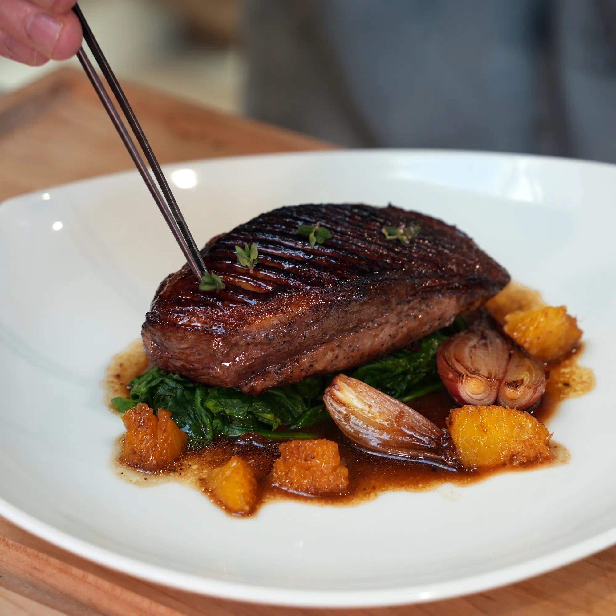 Skin On Magret Duck Breast elegantly plated with wilted greens, roasted shallots, orange segments, and microgreens, showcasing its superior flavor and meaty richness.