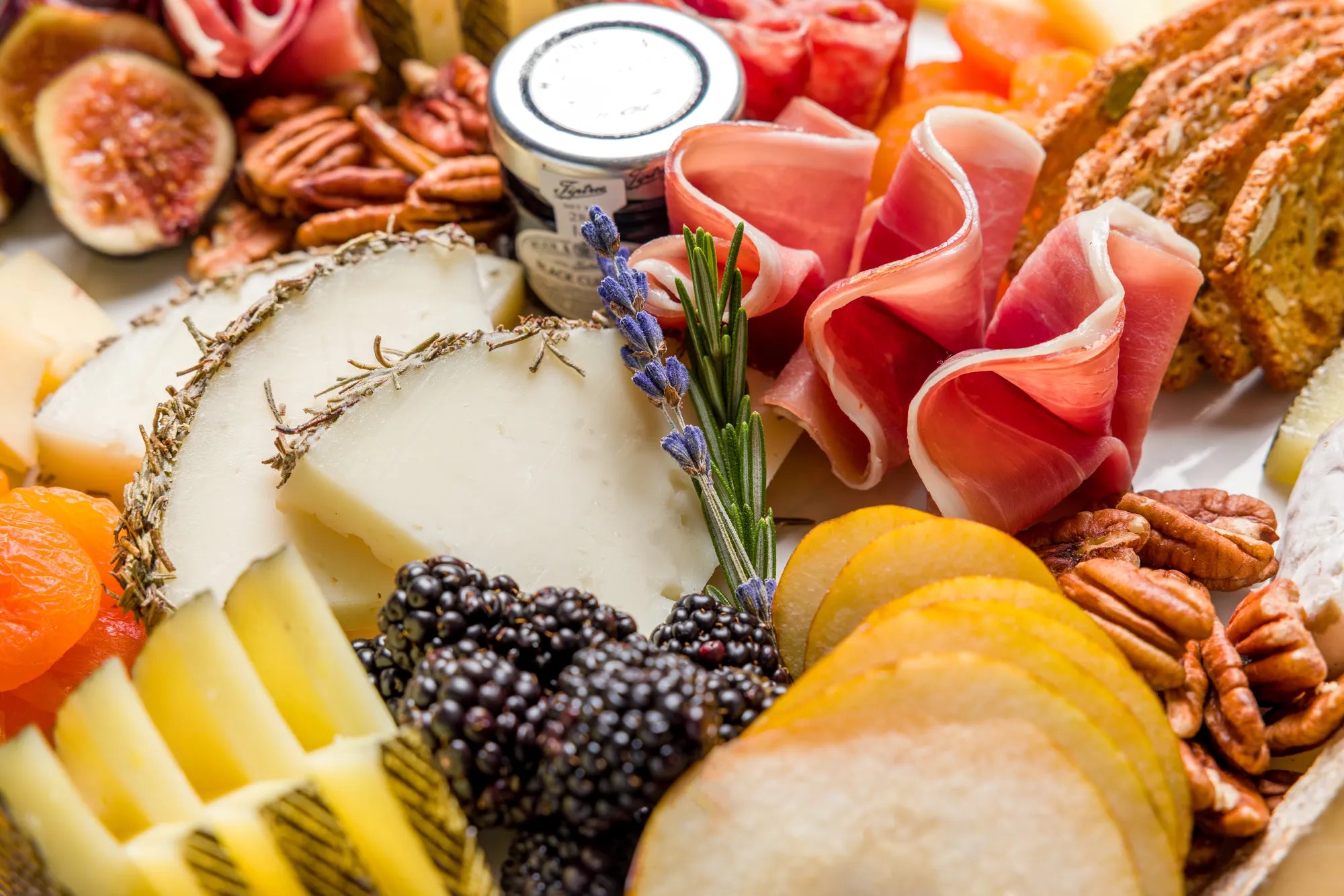 assorted charcuterie with berries and jam jar on white platter