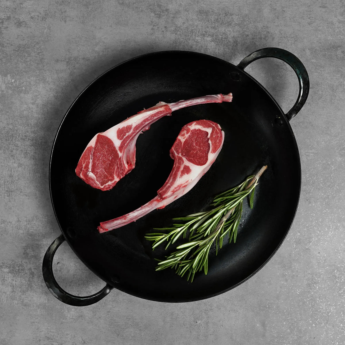 Double Cut Halal Australian Lamb Chop in a black cast-iron pan with rosemary, showcasing French-trimmed bone-in cuts for an elegant presentation.