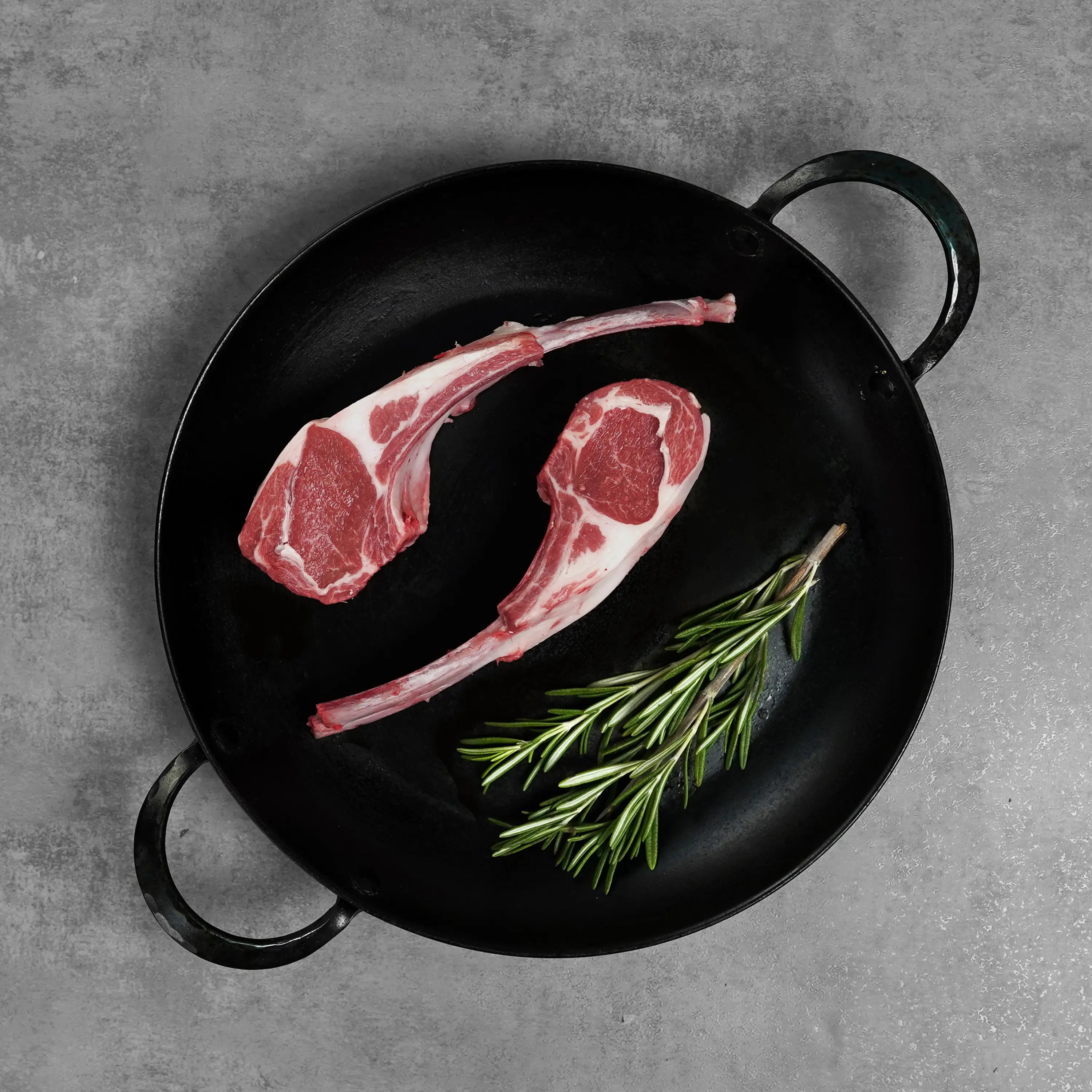 Double Cut Halal Australian Lamb Chop in a black cast-iron pan with rosemary, showcasing French-trimmed bone-in cuts for an elegant presentation.