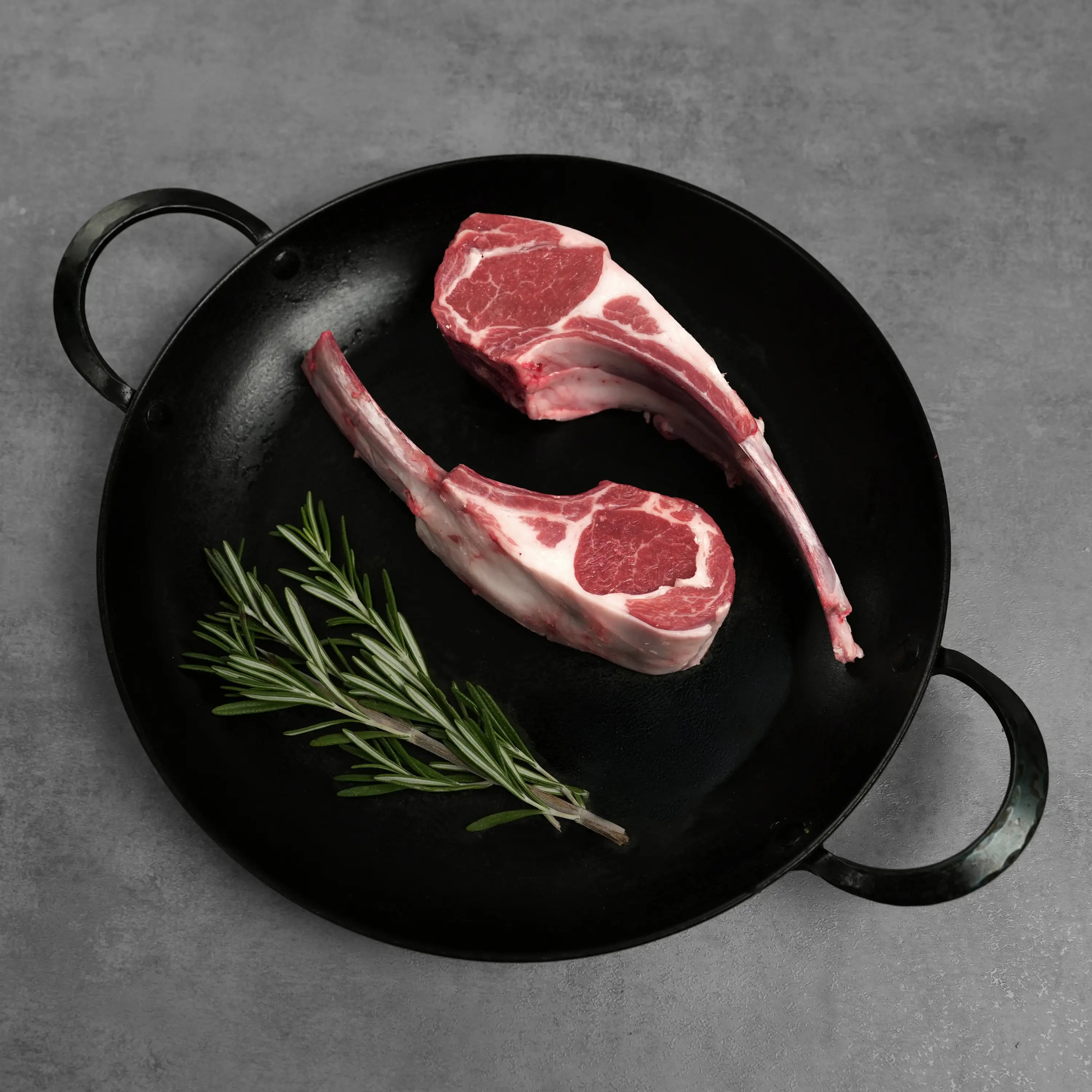 Double Cut Halal Australian Lamb Chop, featuring two raw lollipop-style chops in a black cast-iron pan with fresh rosemary sprigs, ready for cooking.