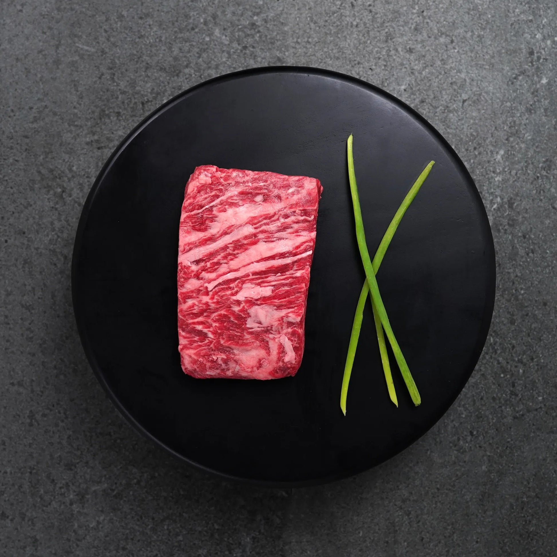 Raw steak on a black plate with green onions on a dark gray background