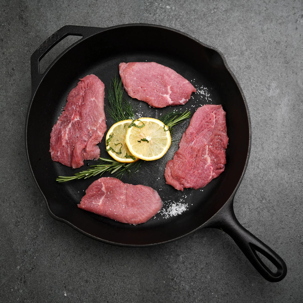 Milk Fed Dutch Veal Scallopine Slices in a skillet with lemon, rosemary, dill, and coarse salt, perfect for dishes like Veal Scallopini Piccata.