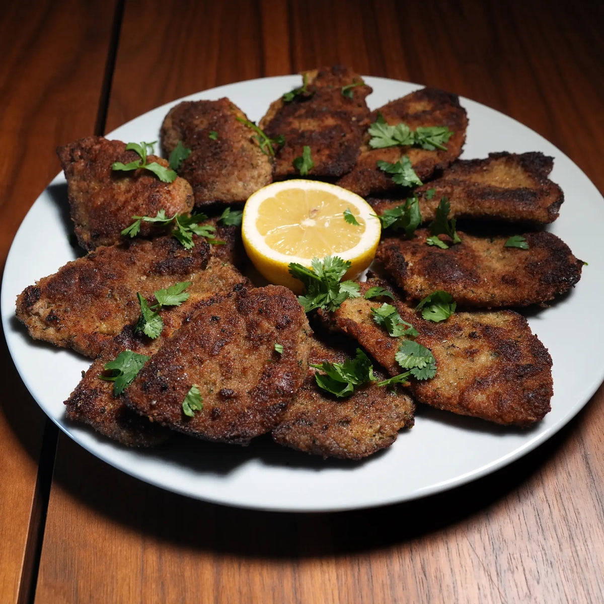 Milk Fed Dutch Veal Scallopine Slices on a white plate, breaded and fried, garnished with herbs and a lemon half for squeezing.