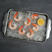 Jumbo Cooked Shrimp arranged on crushed ice with a lemon wedge on a metal tray, showcasing their plumpness and readiness for serving.