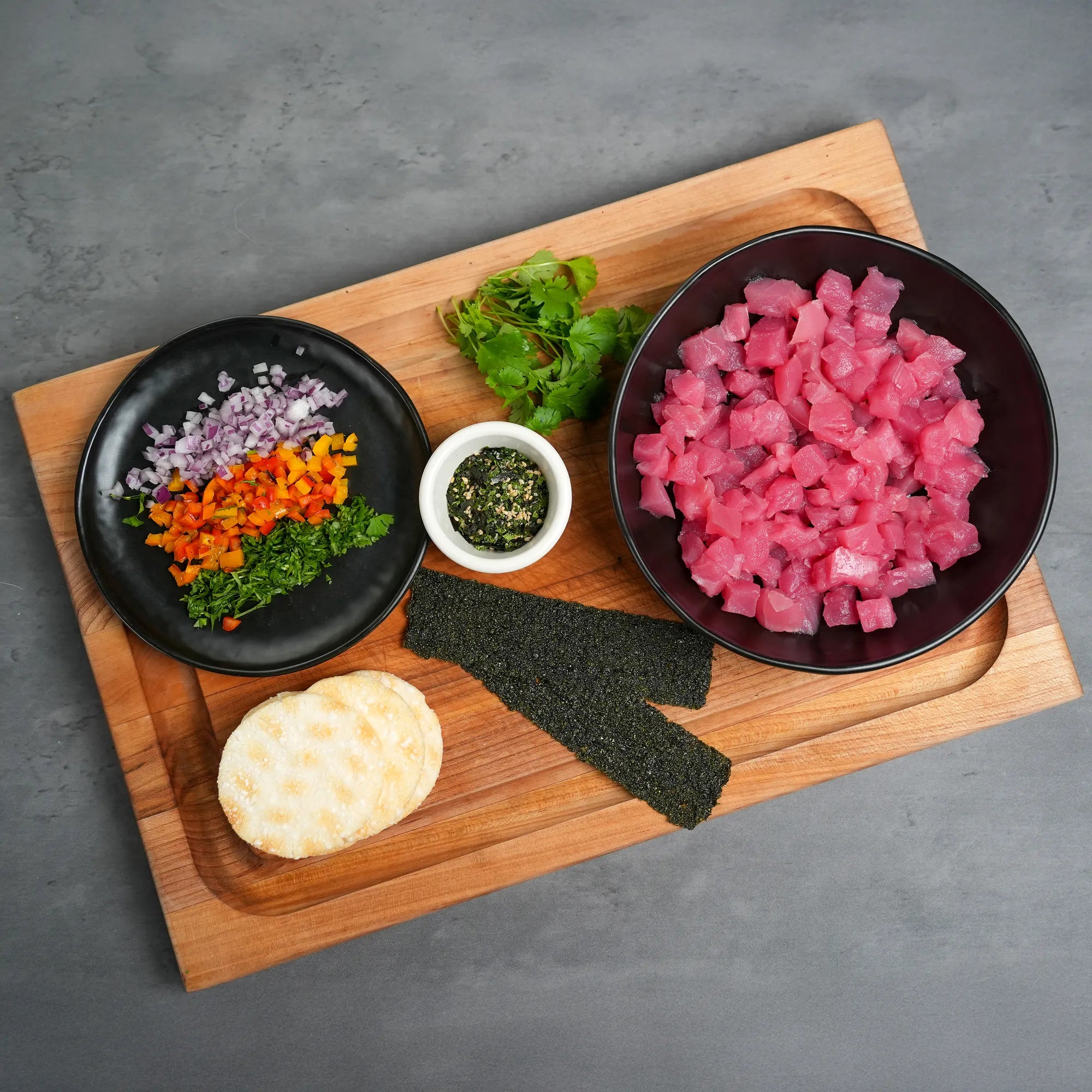 Foley Yellofin Tuna AAA Graded Poke Cubes in a black bowl on a wooden cutting board with sushi roll supplies