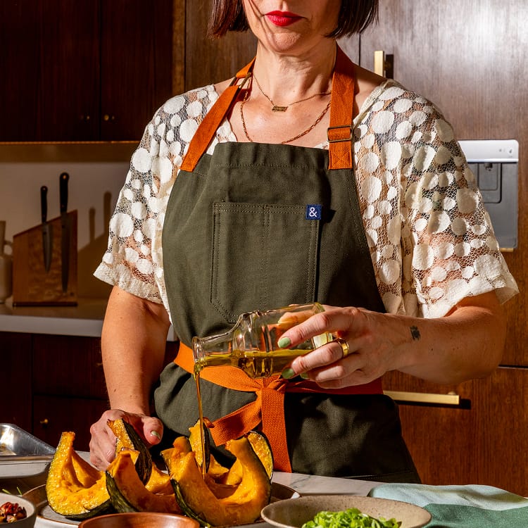 Olive green apron with front pocket, orange straps, and bow at waist