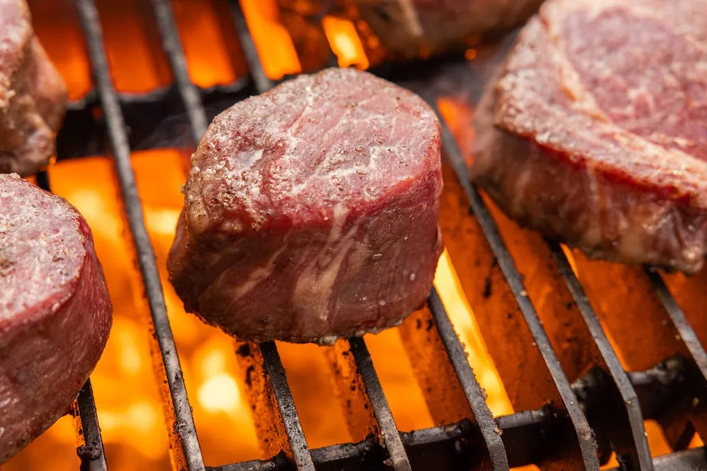 Close-up of beef steaks being grilled on a barbecue with flames.