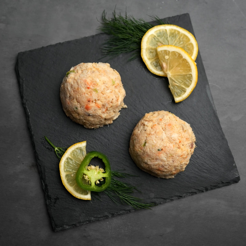 Key West Crab Cakes displayed as three scoops on slate, garnished with dill, lemon wedges, and jalapeño, highlighting their fresh, flavorful seafood composition.