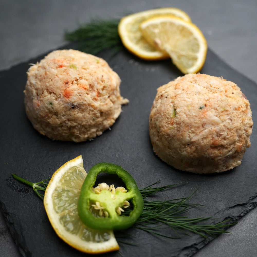 Key West Crab Cakes mixture with lemon wedges, chili slice, and dill garnish on slate board, highlighting fresh, sustainably harvested crab meat and special seasonings.