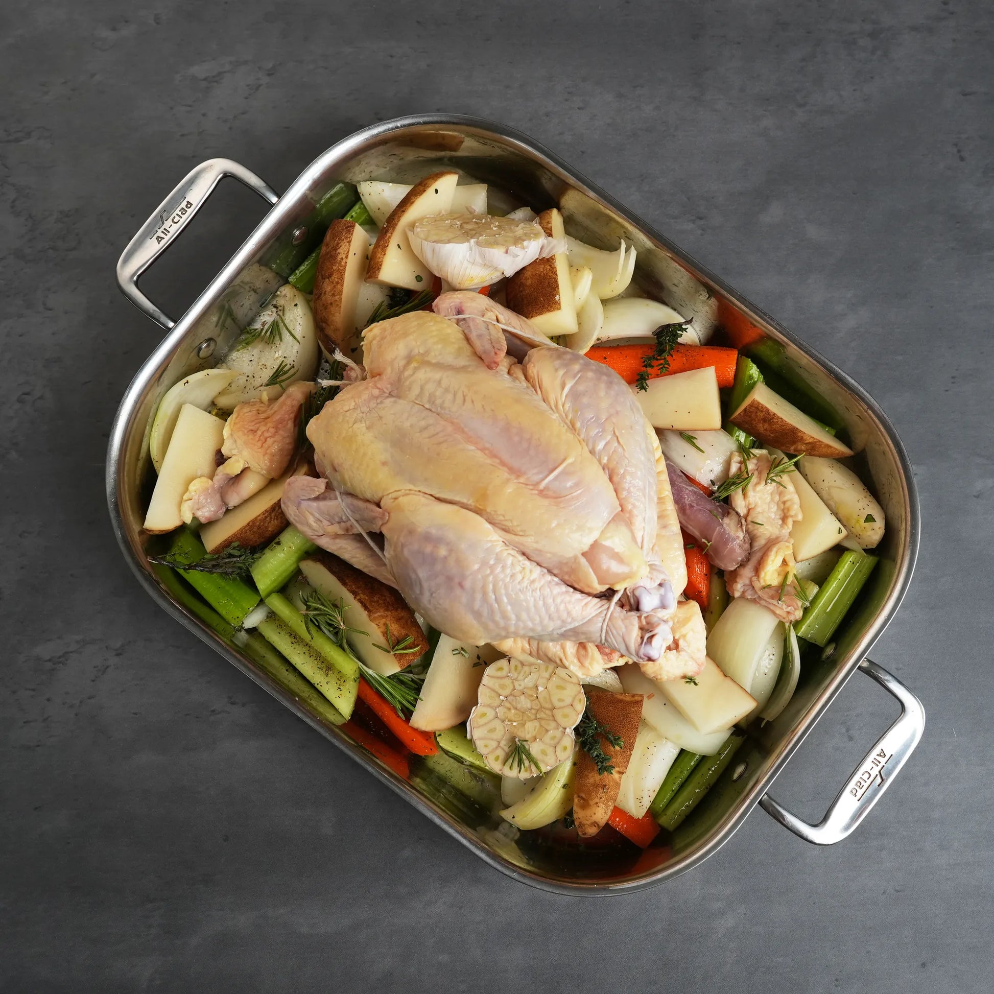 Pasture Raised Heritage Whole Chicken on aromatics in an All-Clad roasting pan, showcasing its preparation for roasting, emphasizing quality and flavor.