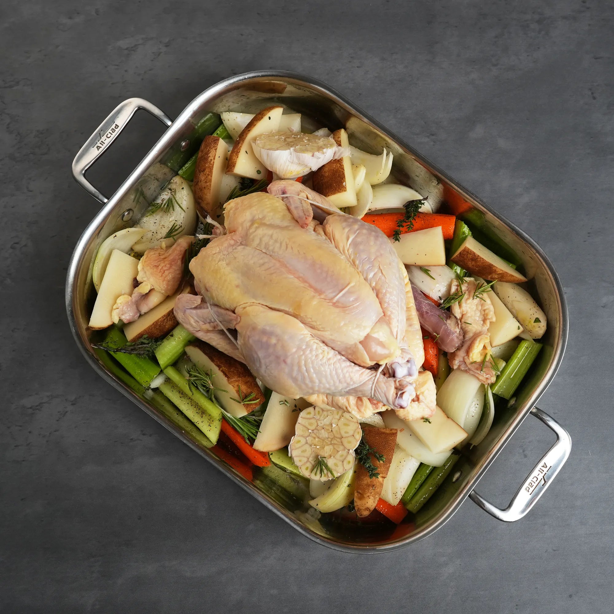 Pasture Raised Heritage Whole Chicken on aromatics in an All-Clad roasting pan, showcasing its preparation for roasting, emphasizing quality and flavor.