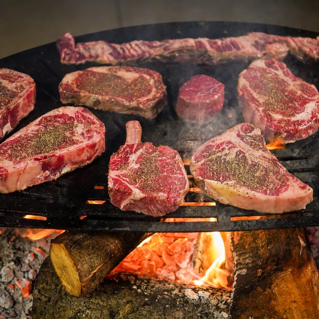 Raw steaks on a grill over an open flame