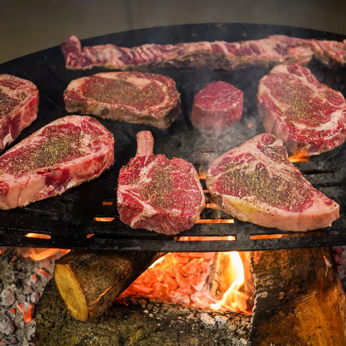Raw steaks on a grill over an open flame
