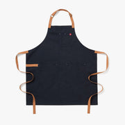 Midnight blue apron with tan adjustable neck straps, two front pockets, and long ties