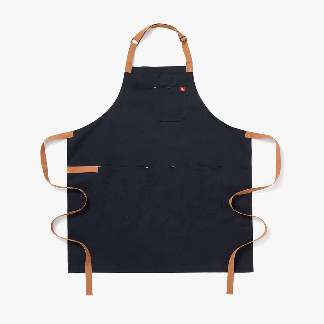 Midnight blue apron with tan adjustable neck straps, two front pockets, and long ties