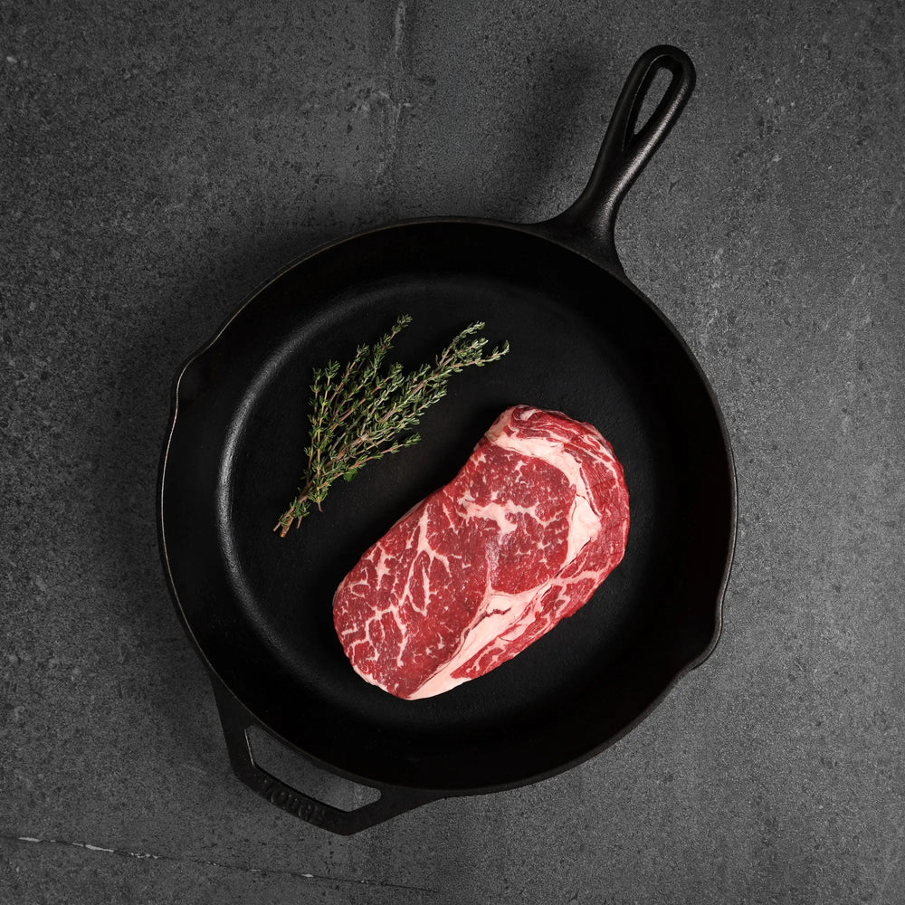 Steak Lovers Prime Combo: A black cast-iron skillet holds a marbled rib-eye steak with fresh thyme, highlighting premium, wet-aged, USDA Prime cuts for ultimate tenderness.