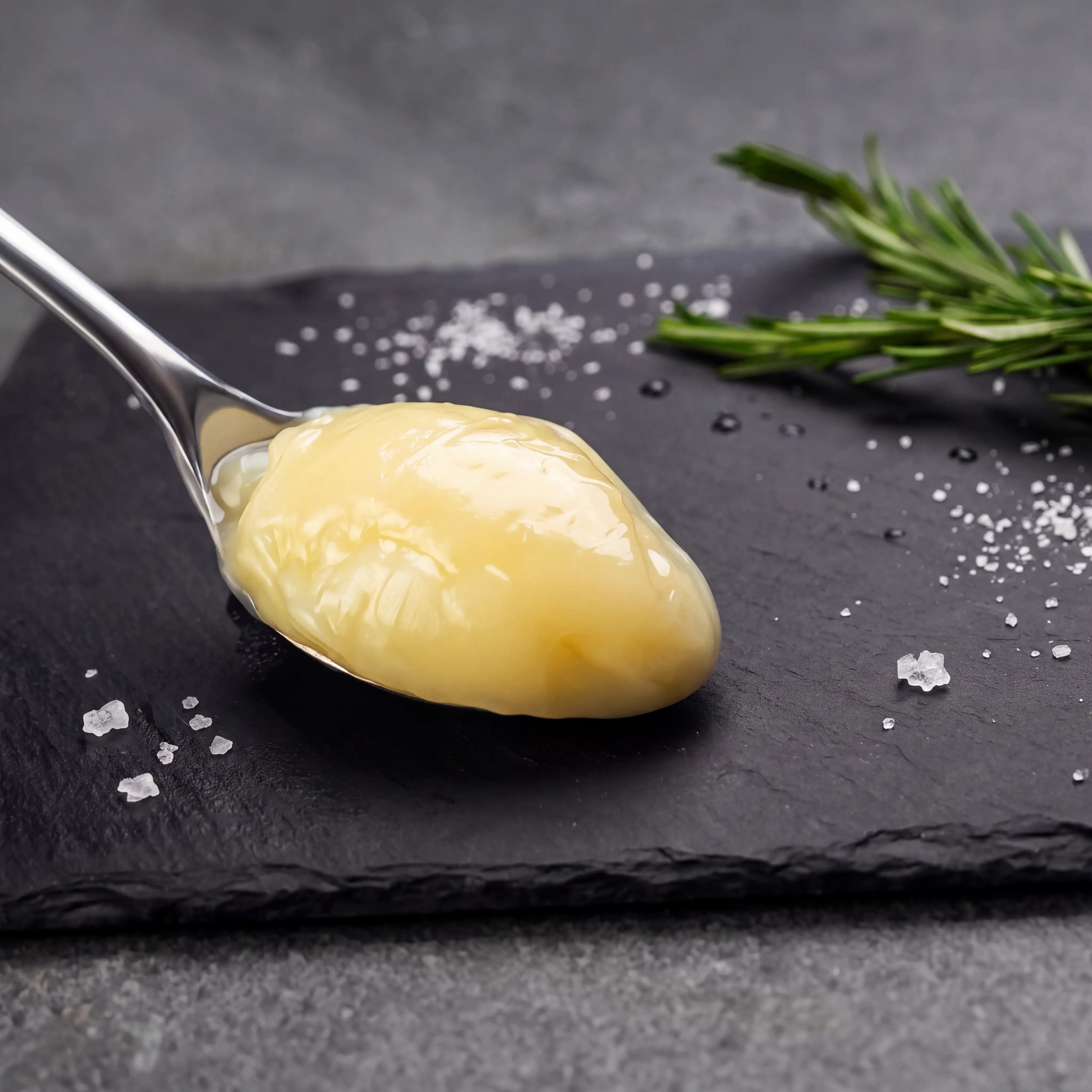 A spoon of creamy sauce on slate, with sea salt flakes and rosemary, highlighting Rendered Duck Fat's rich flavor and high-temperature frying stability.