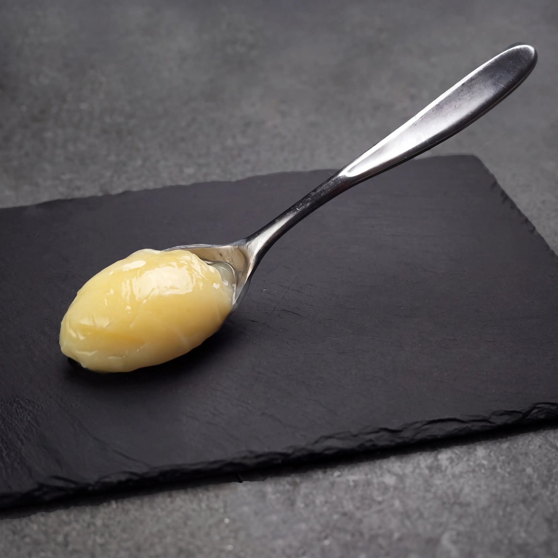 Rendered Duck Fat spooned onto a dark slate surface, illustrating its thick, creamy texture ideal for enhancing flavors in cooking and frying.