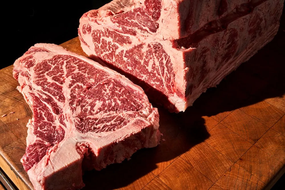 Two raw steak cuts on a wooden cutting board with a dark background