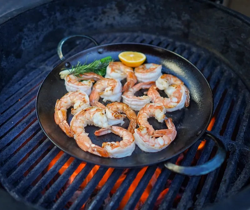 Shrimp being cooked on a grill with a lemon wedge and rosemary.