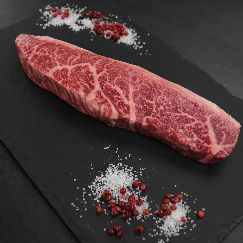 Stone Axe Australian Coulotte Cap Steak on slate, showcasing thick marbling, surrounded by coarse sea salt and pink peppercorns, highlighting premium quality.