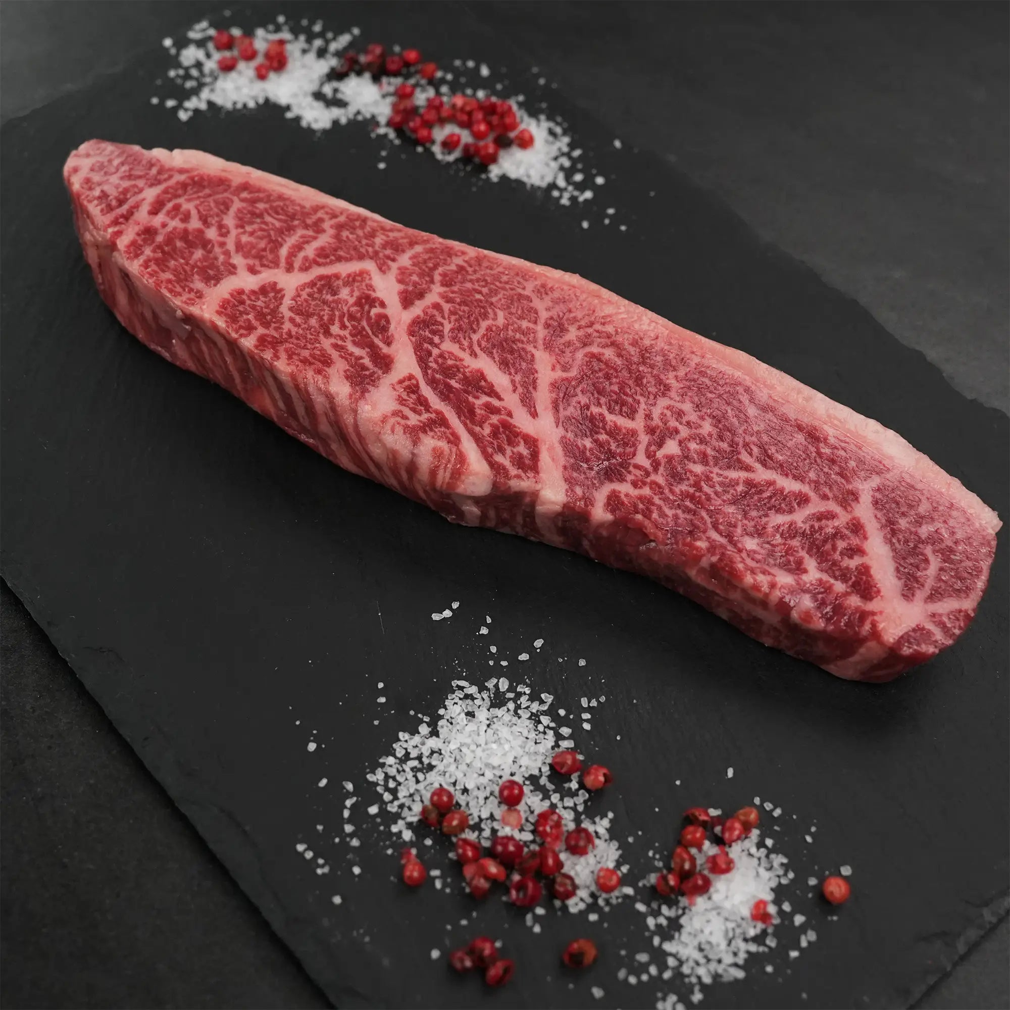 Stone Axe Australian Coulotte Cap Steak on slate, showcasing thick marbling, surrounded by coarse sea salt and pink peppercorns, highlighting premium quality.