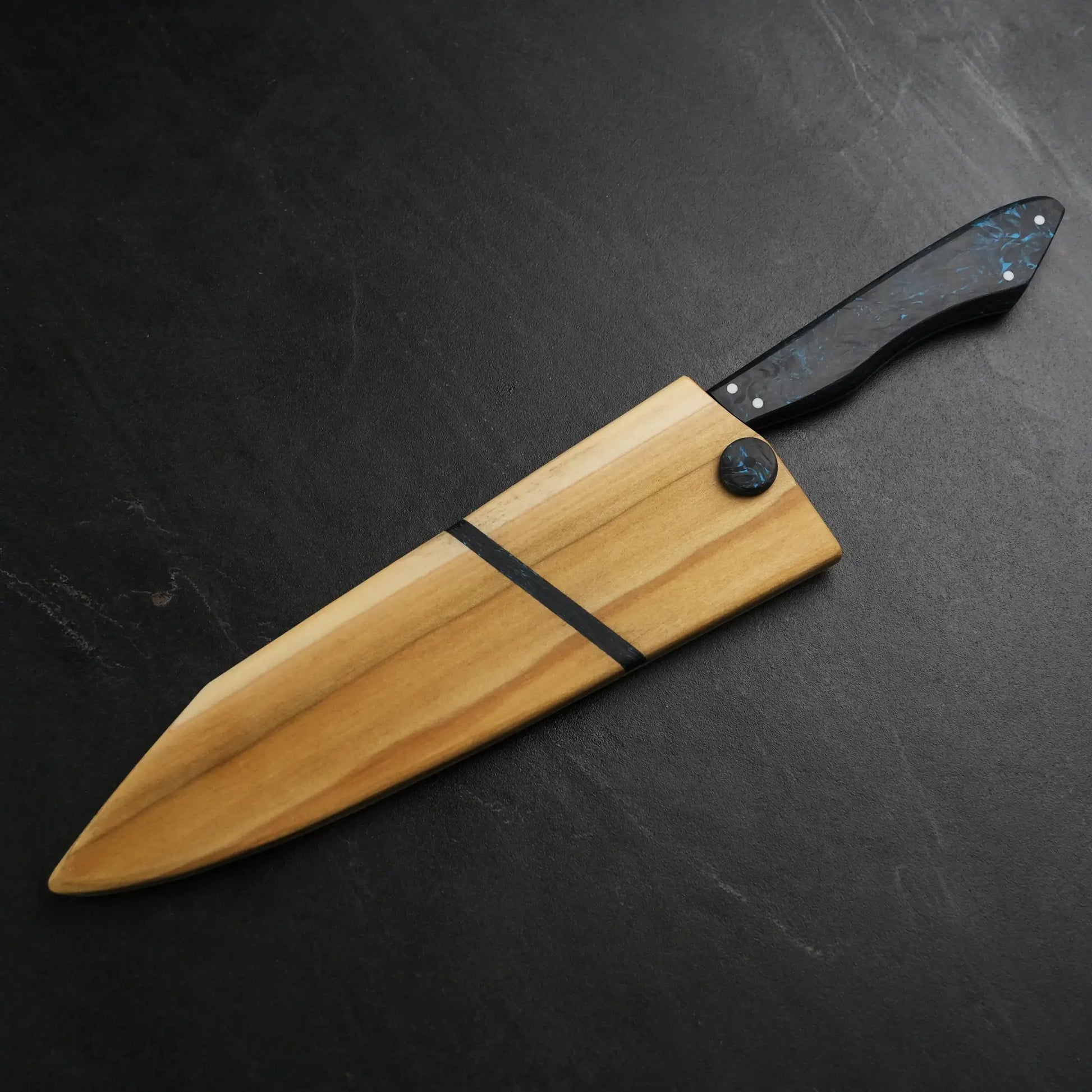 TH Blades Handcrafted 8 Chef Knife with black-and-blue marbled handle in a light wooden scabbard featuring dark inlay stripes, displayed on a dark surface.