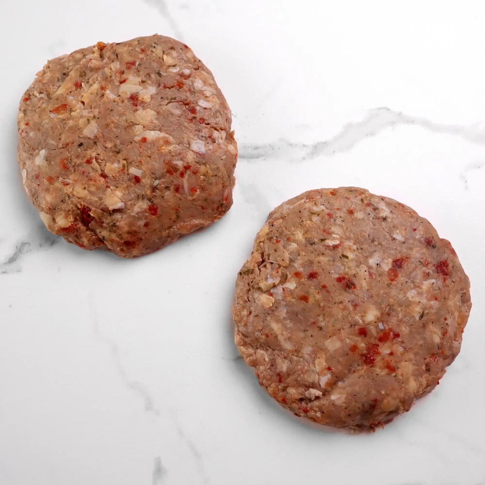 Turkey Burger patties, uncooked and hand-formed, with seasoning and diced peppers and onions, resting on a marble-style countertop, ready for grilling.