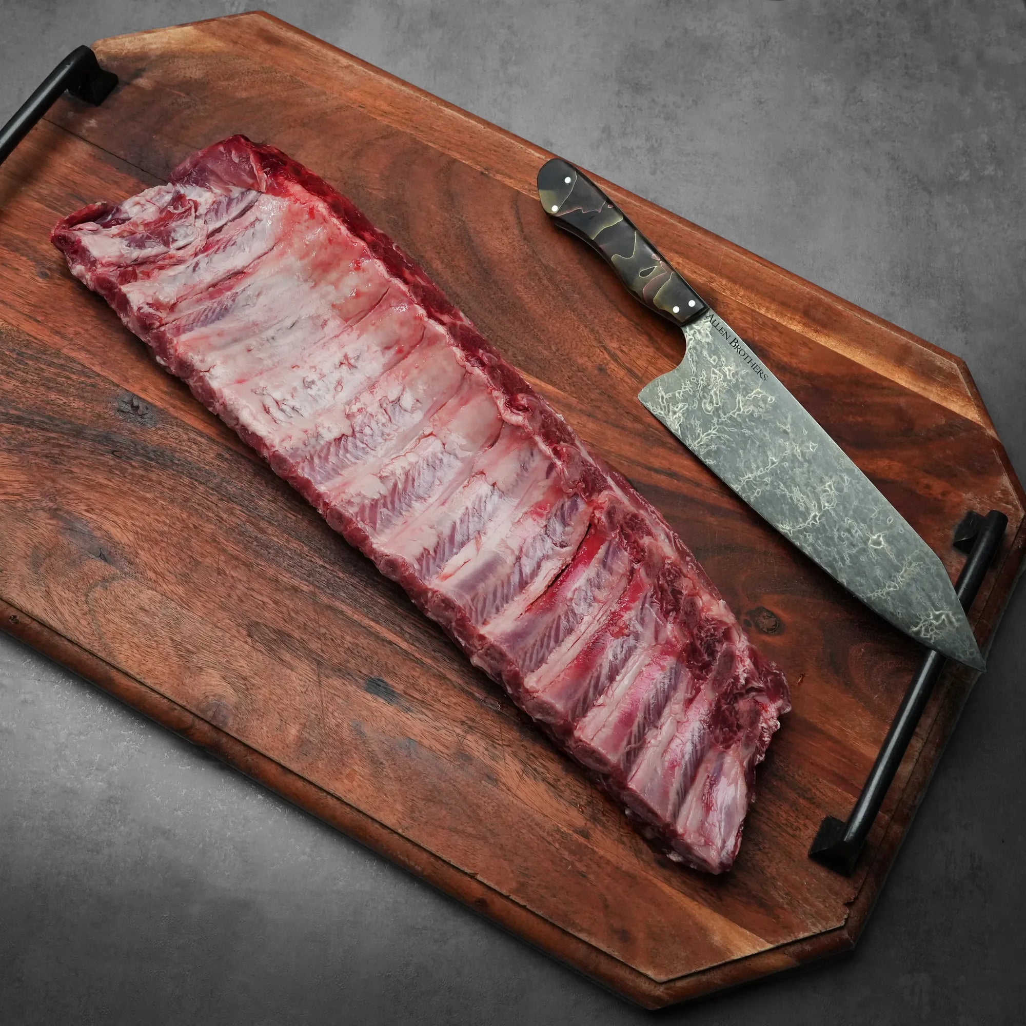 Heritage Duroc Pork Peeled Baby Back Ribs on a wooden board with a cleaver, ready for seasoning and cooking.