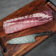 Heritage Duroc Pork Peeled Baby Back Ribs on a wooden board with a Damascus-style knife, ready for seasoning and cooking.