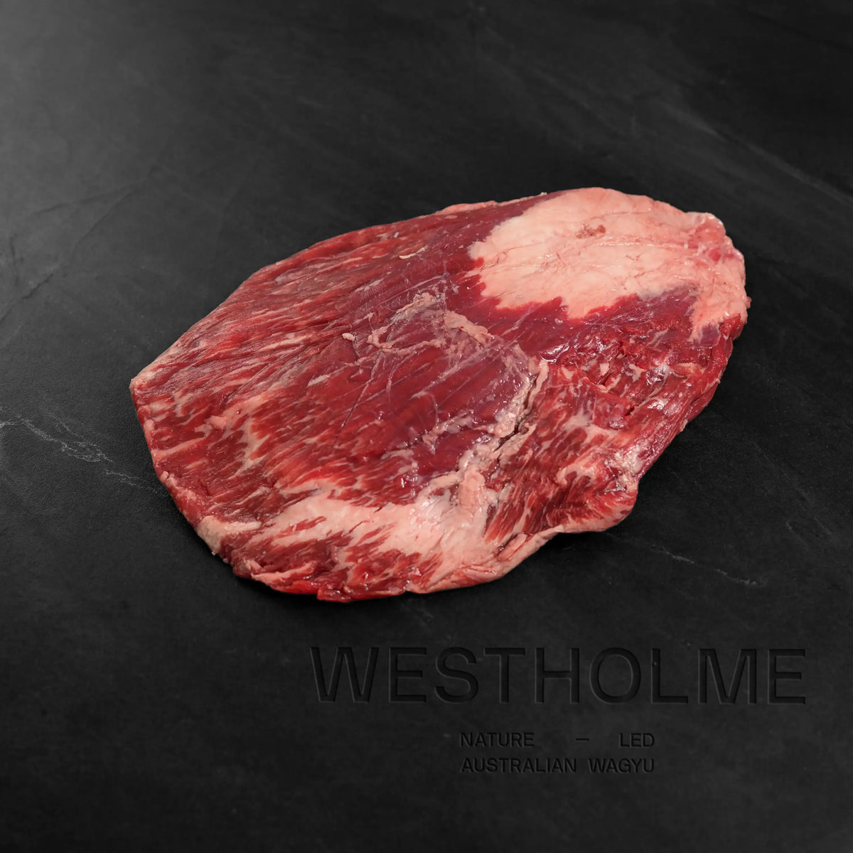 Australian Wagyu Halal Flank Steak, richly marbled, on dark slate surface, branding “WESTHOLME” visible, ideal for various dishes like fajitas and stir-fries.