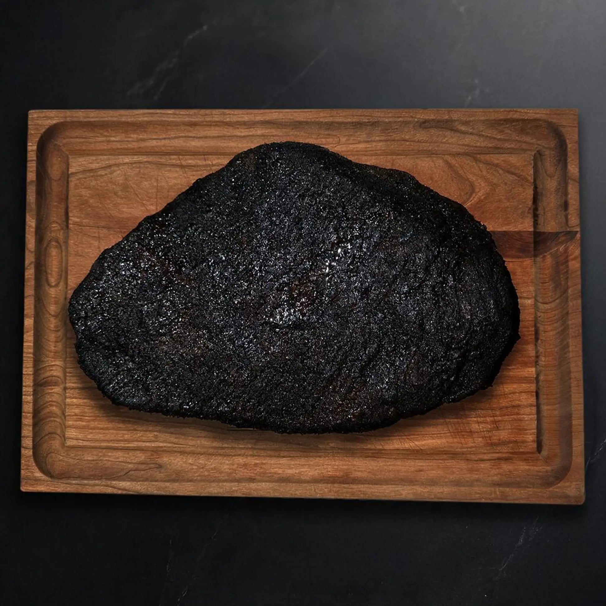 Wagyu Packer Brisket on a wooden board, showcasing its deep, blackened crust from smoking, emphasizing the rich texture and premium quality.
