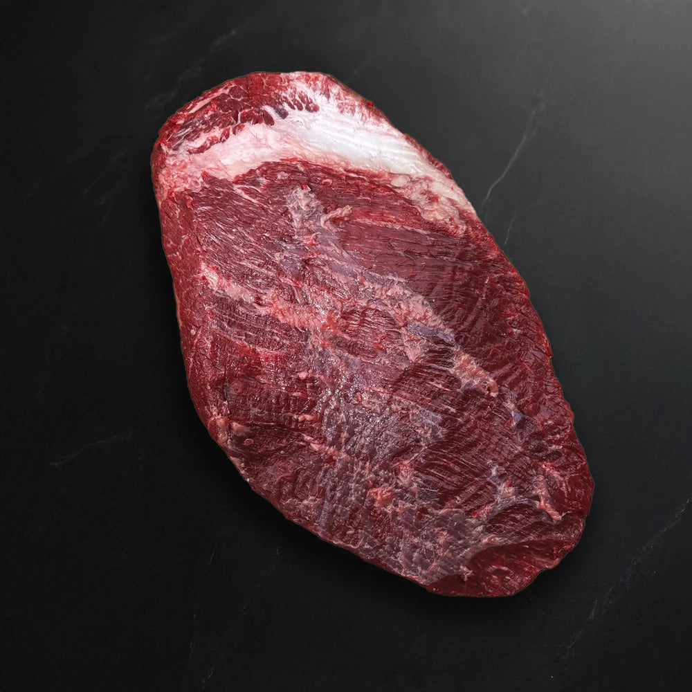 Wagyu Packer Brisket: A large slab of raw beef with deep marbling and a thick fat cap, lying on a dark surface, ready for cooking.