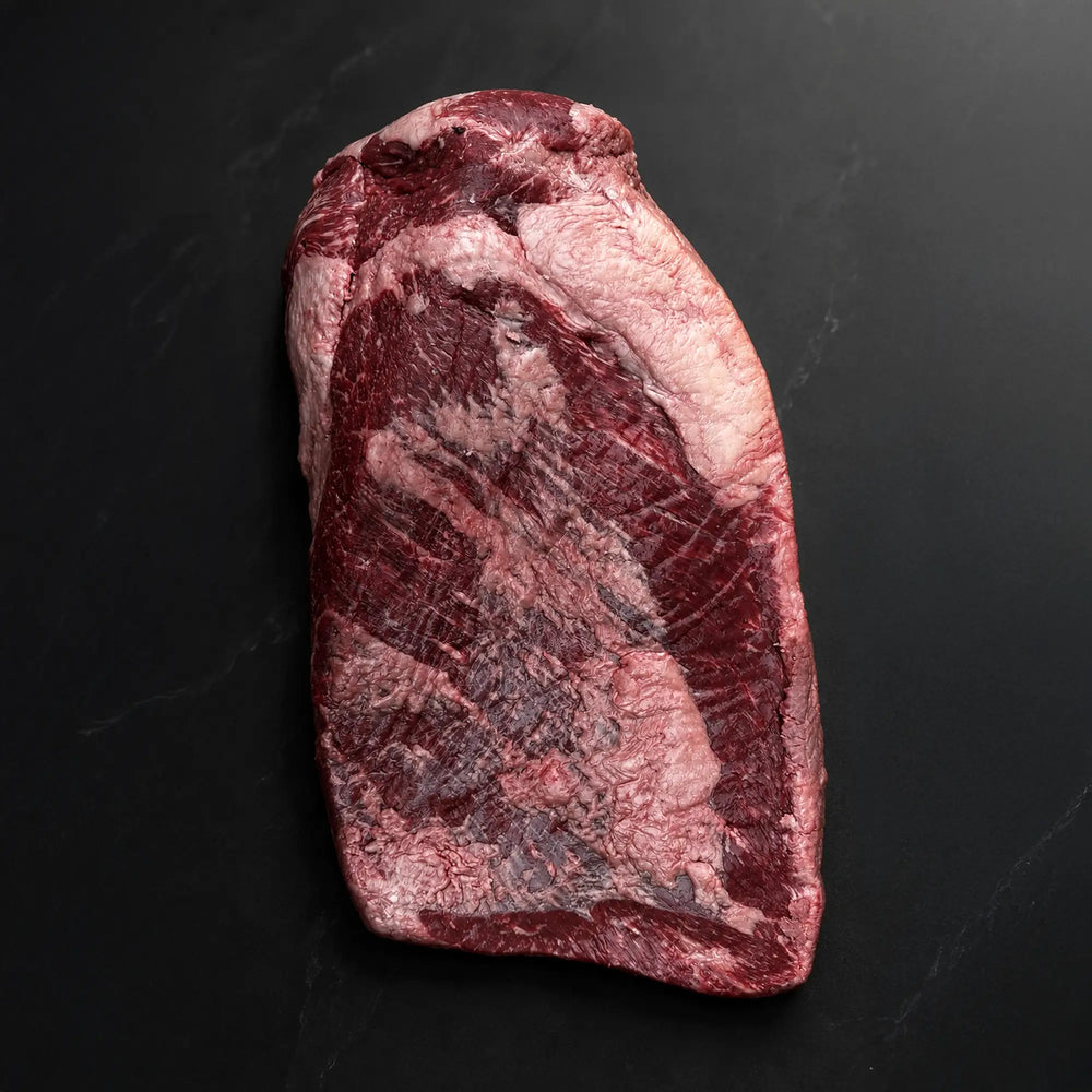 Wagyu Packer Brisket: A raw beef slab with visible muscle and fat cap resting on a dark surface, highlighting its premium quality.