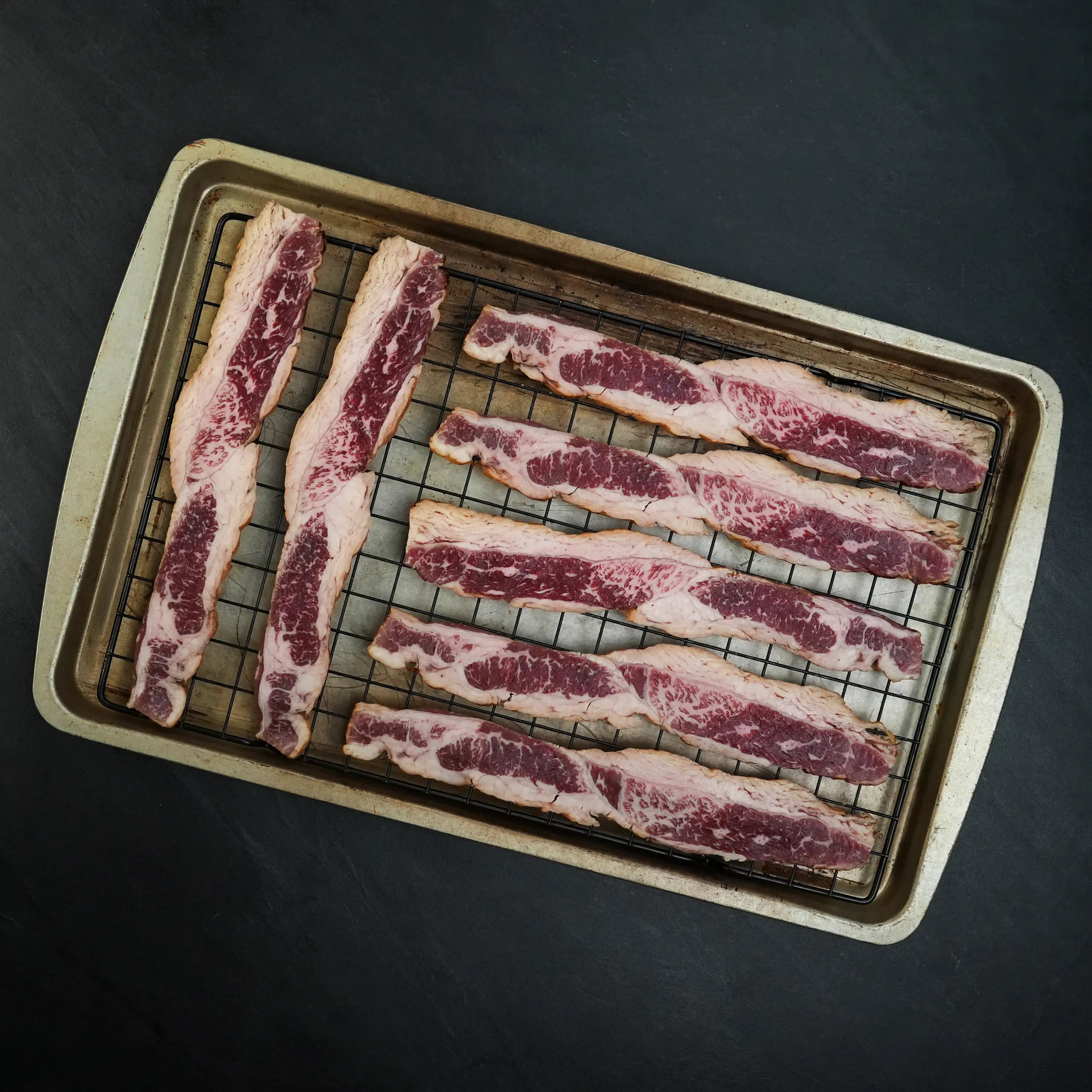 Westholme Australian Wagyu Halal Beef Bacon on a wire rack, showcasing marbled beef strips ready for seasoning, highlighting its richness and robust beefiness.