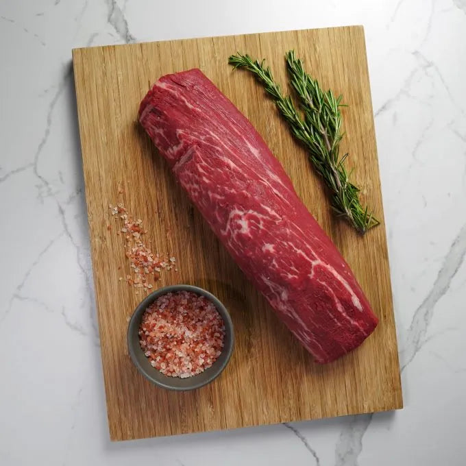 raw meat on wood board with green garnish and pink salt in dark bowl