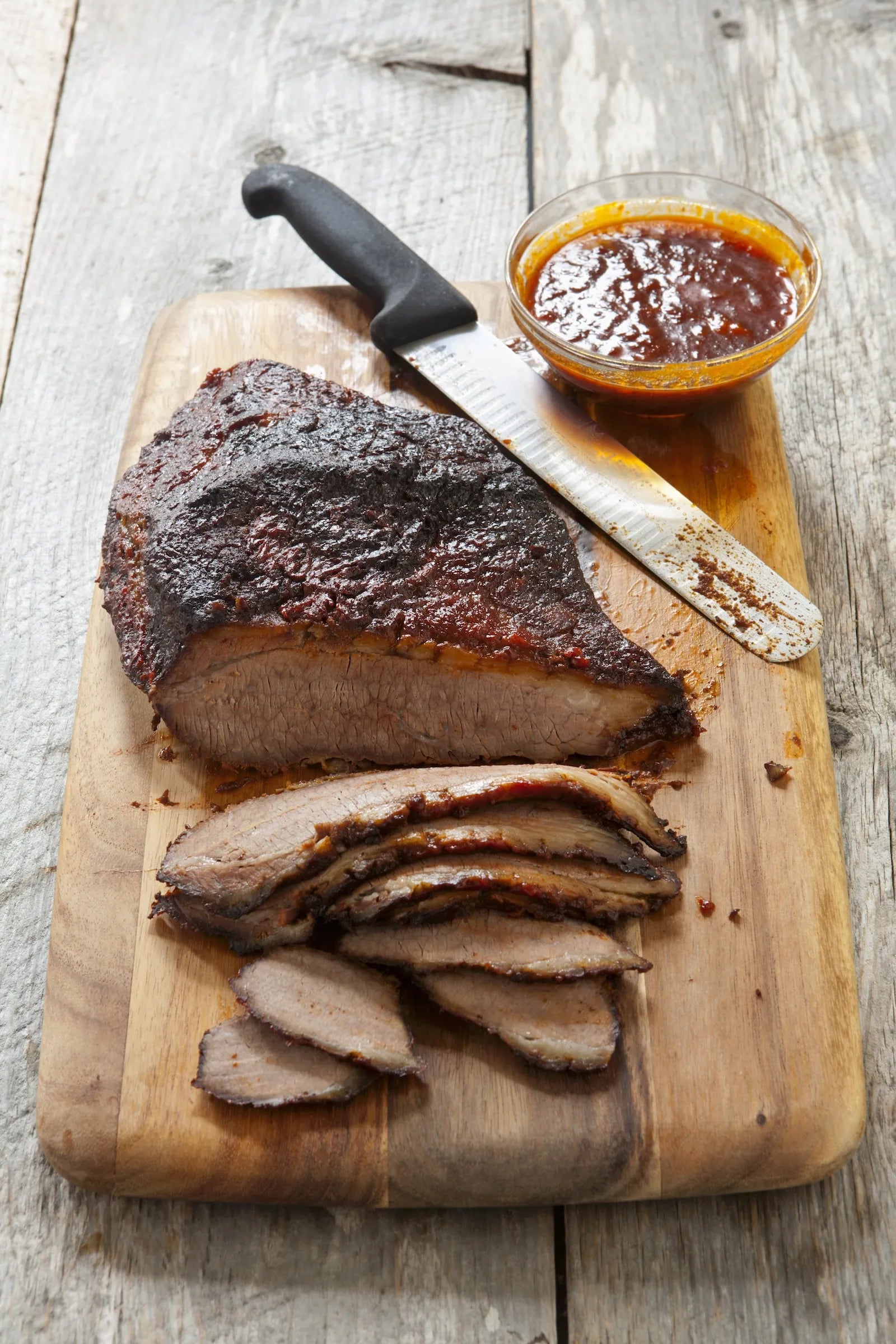 cooked meat on wood board with knife and sauce