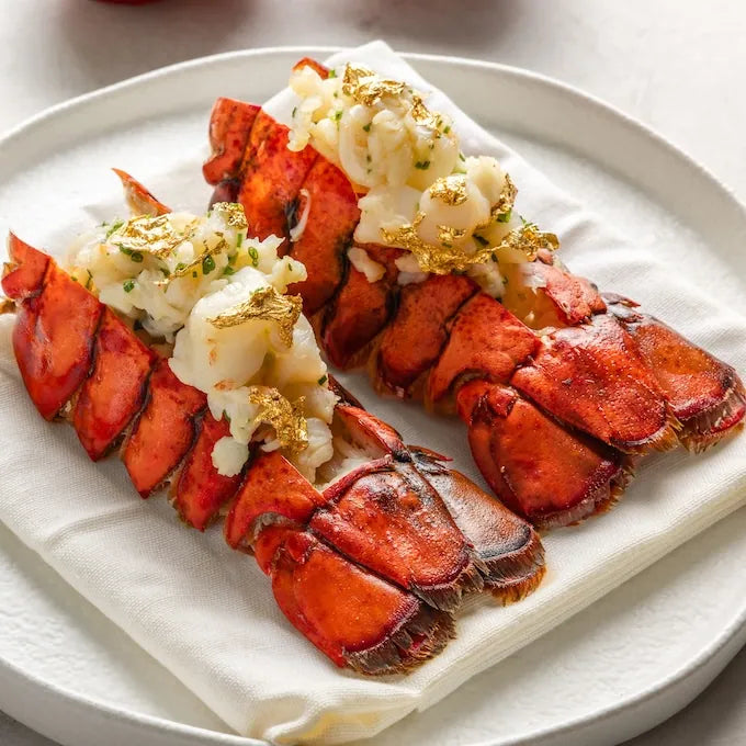 Two lobster tails on a white plate with gold flakes.