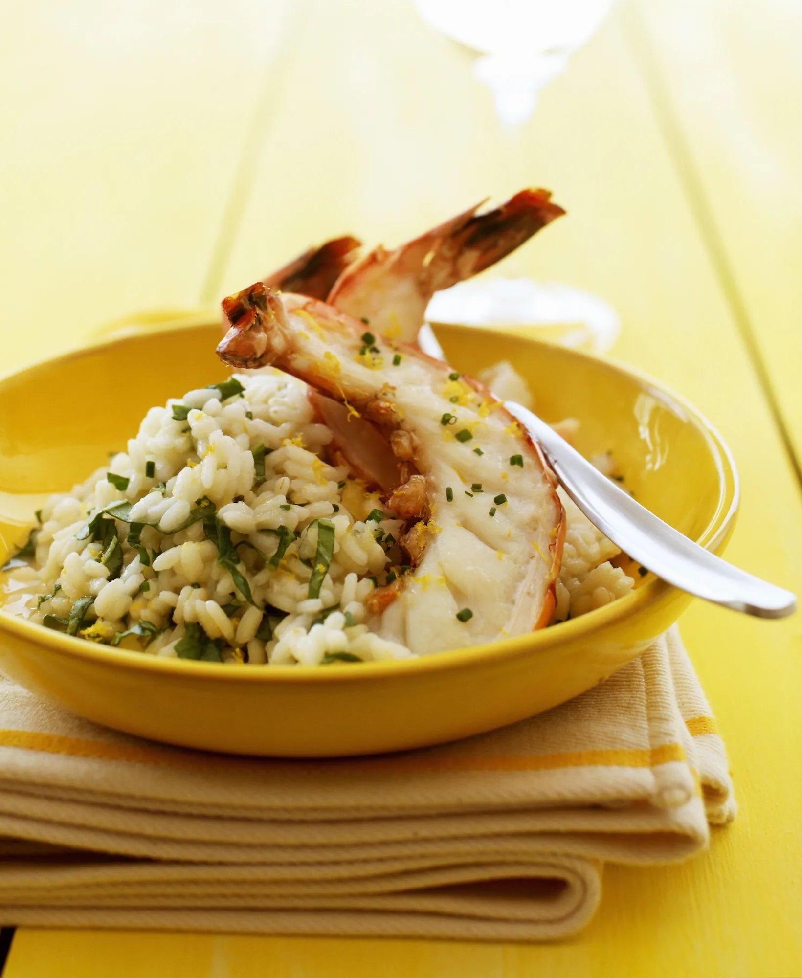 Yellow bowl with seafood dish and a spoon on a yellow background
