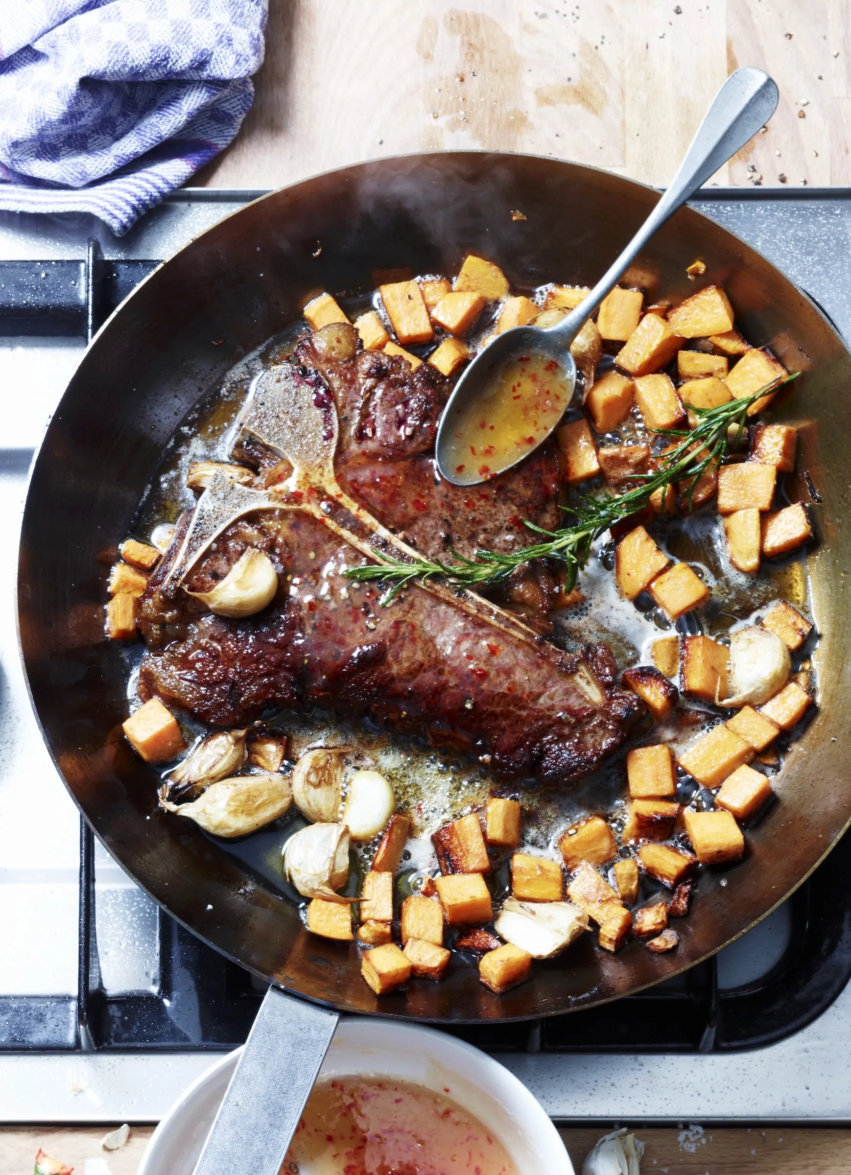 Steak with roasted potatoes in a frying pan on a stove