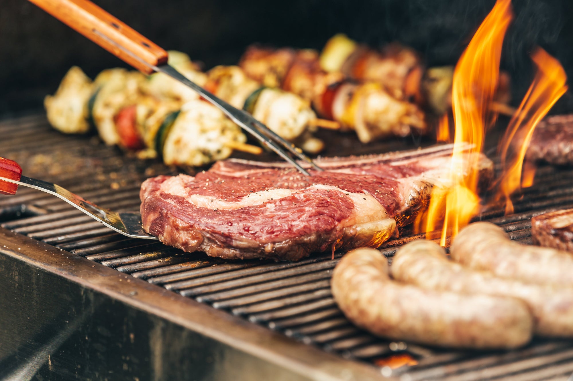 steaks and sausages on grill with flames